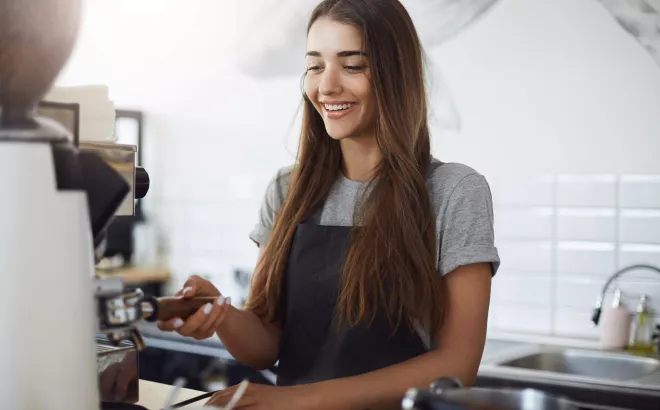 Glimlachende jonge vrouw werkt als barista in een koffiebar